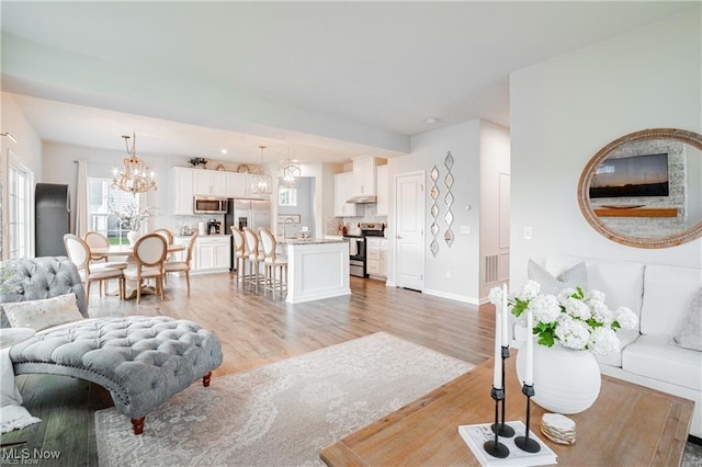 living room with visible vents, light wood-style flooring, baseboards, and an inviting chandelier