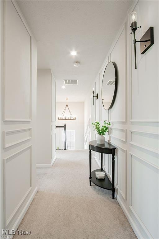 hall featuring visible vents, carpet flooring, an upstairs landing, and a decorative wall