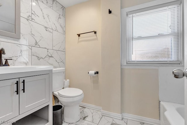 bathroom featuring toilet, vanity, baseboards, marble finish floor, and a tub