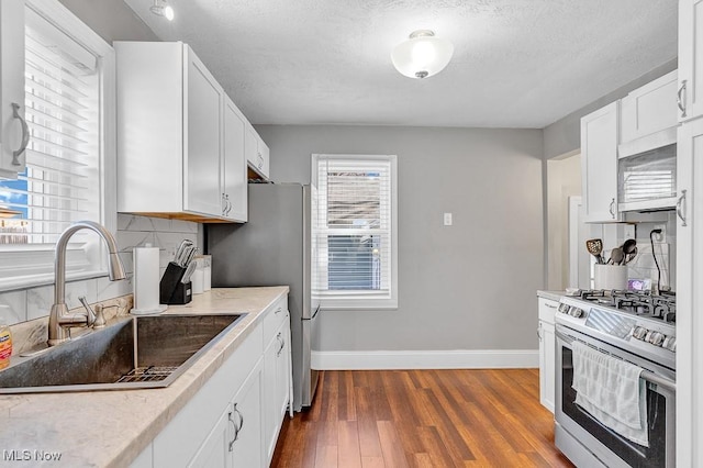 kitchen featuring baseboards, decorative backsplash, appliances with stainless steel finishes, dark wood-type flooring, and a sink