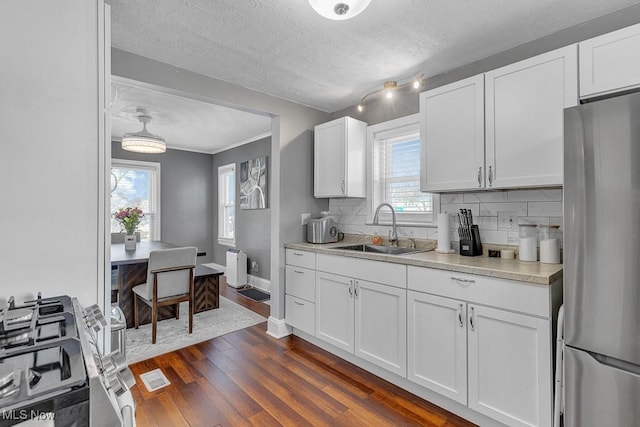 kitchen with a sink, light countertops, freestanding refrigerator, decorative backsplash, and dark wood-style floors