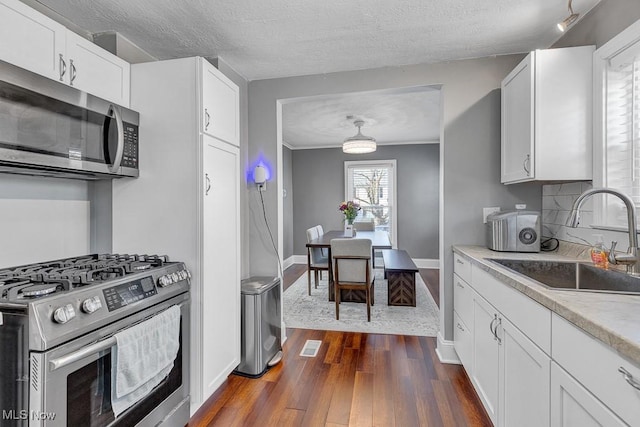 kitchen with dark wood finished floors, light countertops, appliances with stainless steel finishes, white cabinets, and a sink