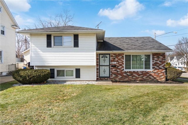 split level home featuring brick siding, a shingled roof, and a front yard