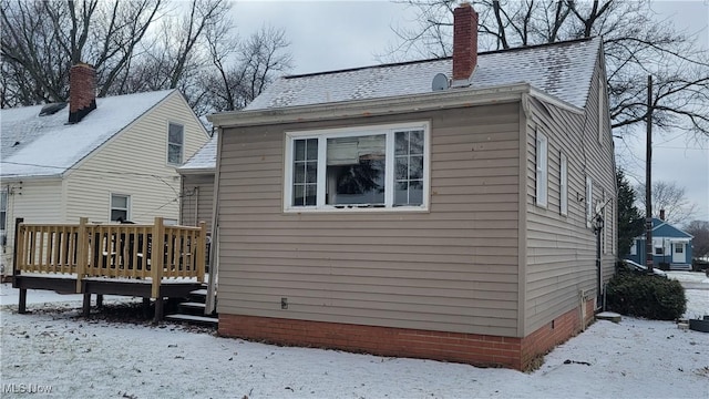 snow covered house with a shingled roof, a chimney, and a deck