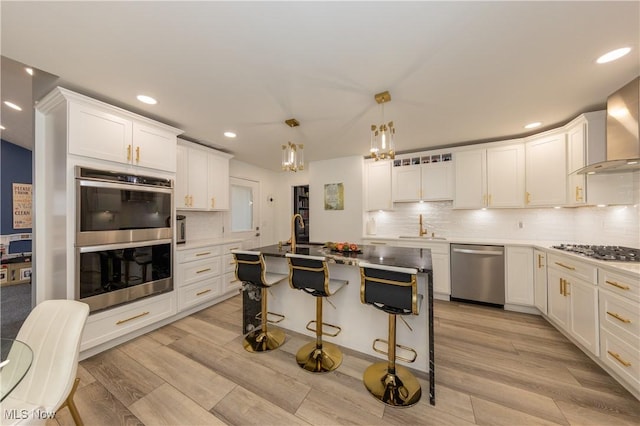 kitchen featuring a breakfast bar area, light wood-style floors, white cabinets, appliances with stainless steel finishes, and wall chimney range hood