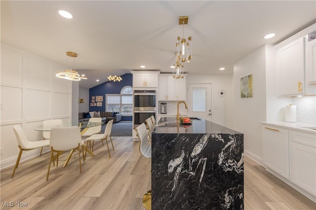 kitchen featuring white cabinets, light wood finished floors, decorative backsplash, and stainless steel double oven