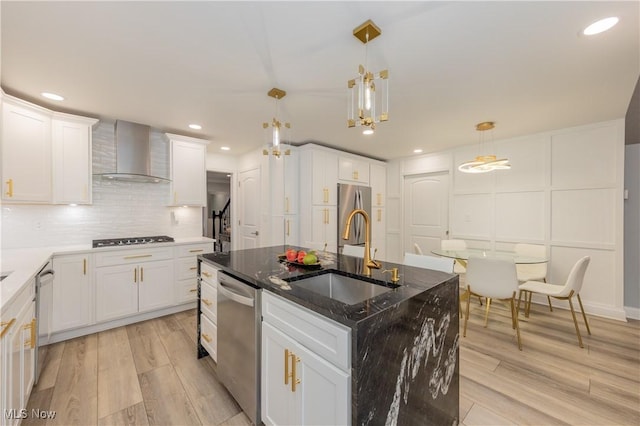 kitchen with a sink, appliances with stainless steel finishes, decorative backsplash, wall chimney exhaust hood, and a center island with sink