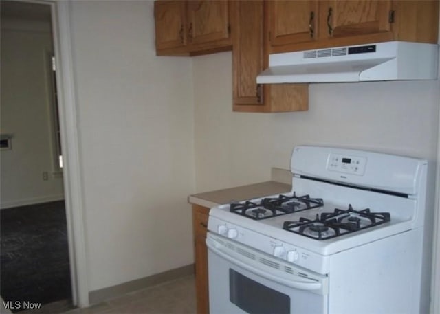 kitchen featuring white range with gas cooktop, baseboards, brown cabinetry, light countertops, and under cabinet range hood