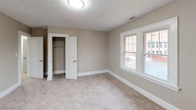 unfurnished bedroom with baseboards, visible vents, light colored carpet, a textured ceiling, and a closet