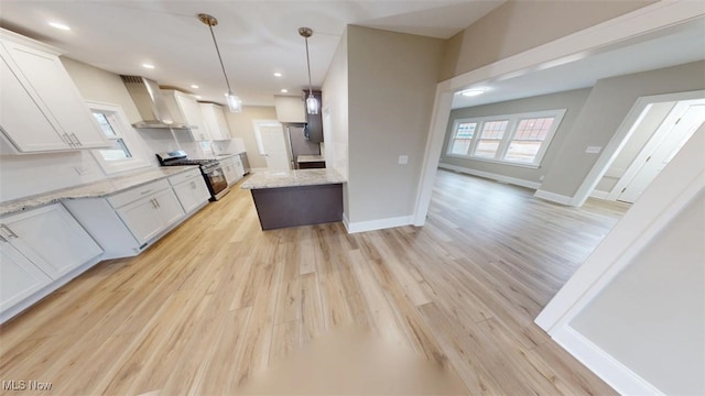 kitchen featuring gas range, white cabinetry, light wood-style floors, and wall chimney range hood