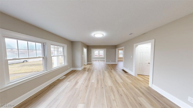 unfurnished living room with light wood-style floors, visible vents, a textured ceiling, and baseboards