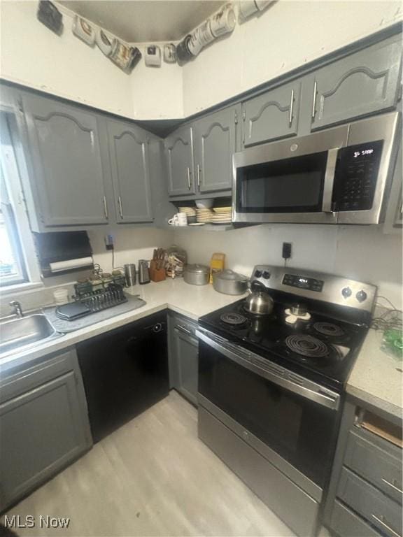 kitchen with appliances with stainless steel finishes, gray cabinets, light countertops, and a sink