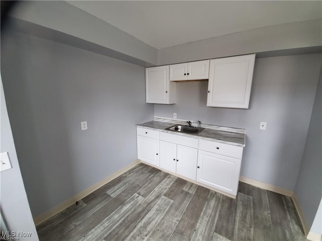 kitchen with a sink, wood finished floors, white cabinetry, and baseboards