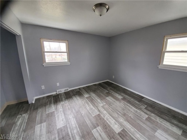 unfurnished room featuring baseboards, visible vents, and dark wood-type flooring