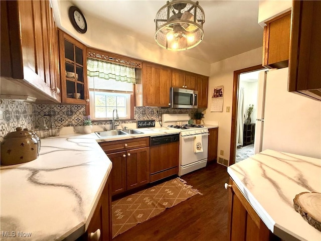 kitchen featuring decorative backsplash, glass insert cabinets, brown cabinetry, a sink, and white appliances