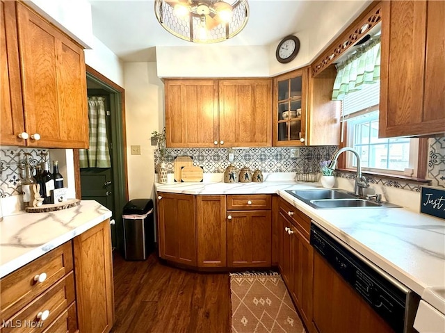 kitchen with brown cabinets, light countertops, decorative backsplash, a sink, and dishwashing machine