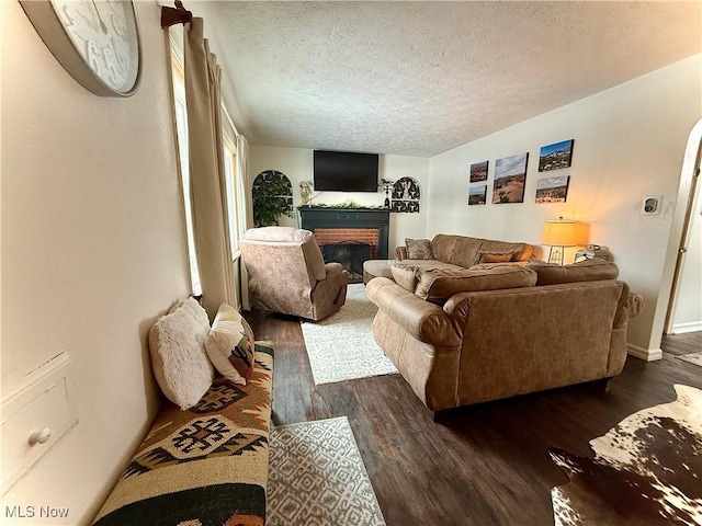 living room featuring a textured ceiling, a brick fireplace, dark wood finished floors, and baseboards