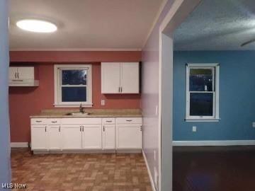 kitchen with light countertops, white cabinets, a sink, and baseboards