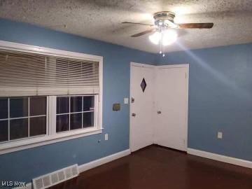 interior space featuring a ceiling fan, visible vents, a textured ceiling, and baseboards