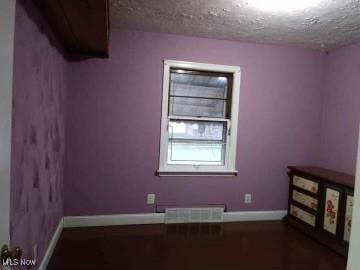 empty room featuring a textured ceiling, wood finished floors, visible vents, and baseboards