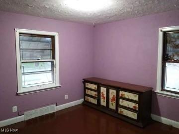 empty room with visible vents, a textured ceiling, and baseboards