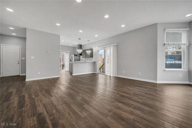 unfurnished living room featuring baseboards, dark wood-type flooring, and recessed lighting