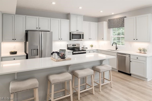 kitchen featuring tasteful backsplash, a breakfast bar area, appliances with stainless steel finishes, light wood-style floors, and a sink