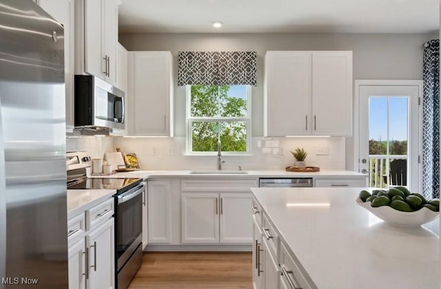 kitchen featuring light countertops, decorative backsplash, appliances with stainless steel finishes, light wood-style floors, and white cabinets