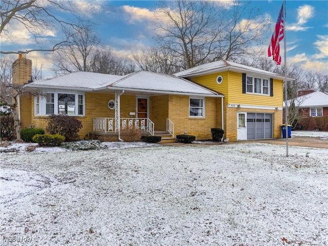 tri-level home featuring brick siding, a chimney, a porch, an attached garage, and driveway