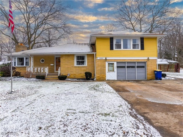 split level home with driveway, a chimney, an attached garage, a porch, and brick siding