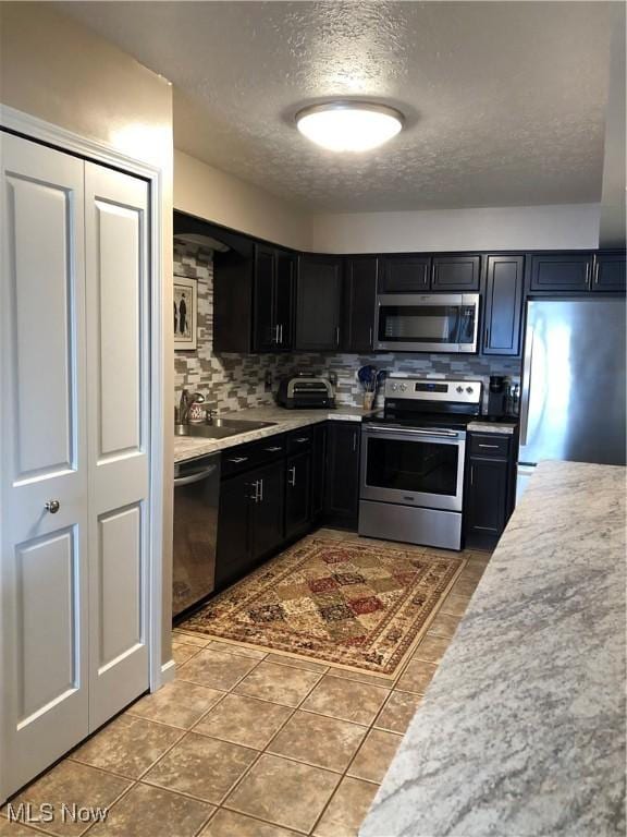 kitchen with stainless steel appliances, light countertops, backsplash, a sink, and dark cabinetry