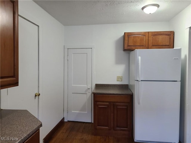 kitchen with dark countertops, dark wood-style floors, brown cabinets, freestanding refrigerator, and a textured ceiling