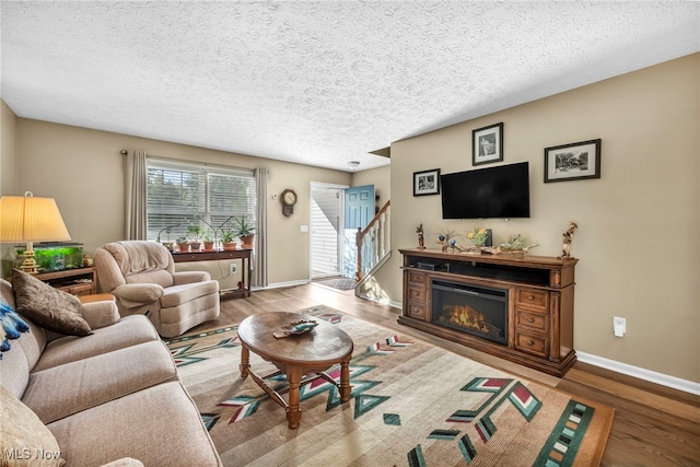 living room with a textured ceiling, wood finished floors, baseboards, stairway, and a glass covered fireplace