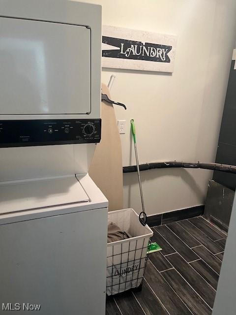 laundry room with laundry area, wood finish floors, stacked washing maching and dryer, and baseboards