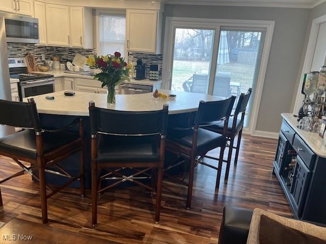 kitchen with a kitchen breakfast bar, stainless steel appliances, dark wood finished floors, and white cabinets