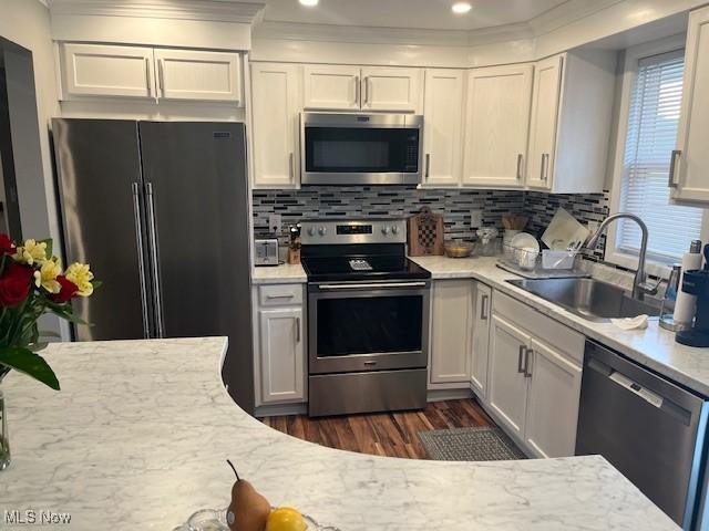 kitchen featuring dark wood-type flooring, a sink, white cabinets, appliances with stainless steel finishes, and backsplash