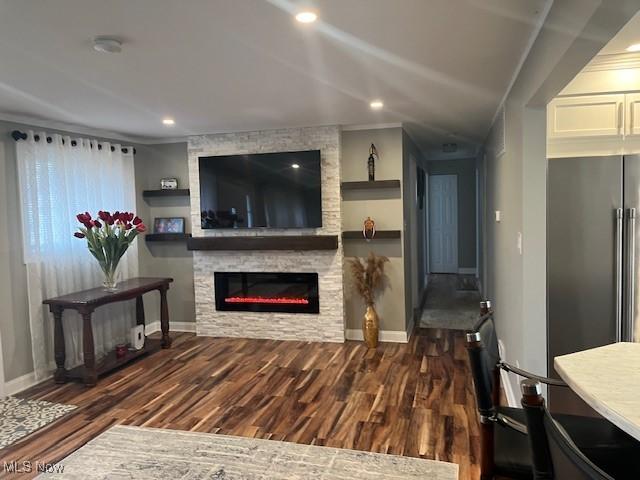 living room featuring recessed lighting, baseboards, dark wood-type flooring, and a stone fireplace