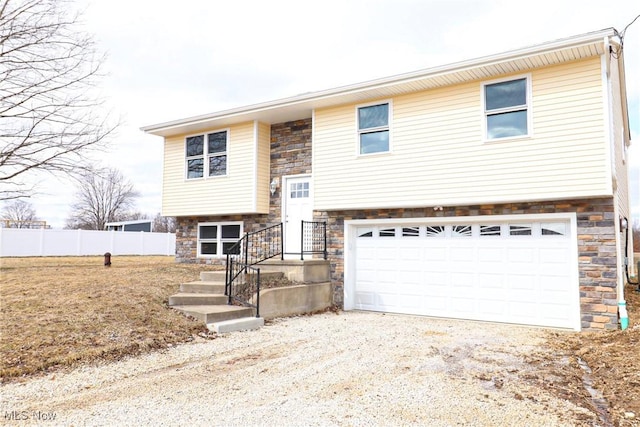 split foyer home featuring a garage, stone siding, and fence