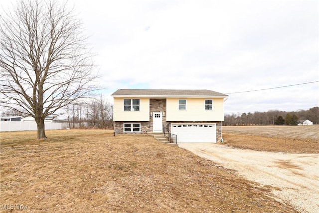 bi-level home with dirt driveway, stone siding, and a garage