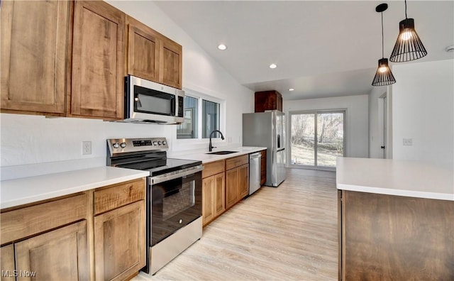 kitchen with light wood-style flooring, hanging light fixtures, vaulted ceiling, stainless steel appliances, and a sink