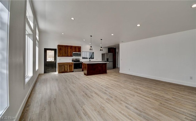 kitchen featuring stainless steel appliances, a kitchen island, baseboards, open floor plan, and light wood-style floors