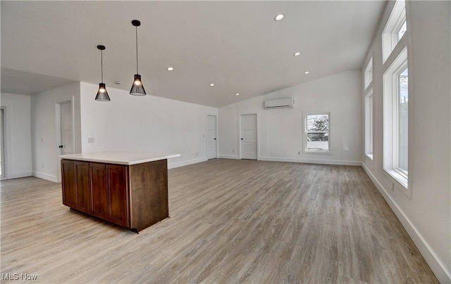 kitchen with a wall unit AC, light wood-style flooring, a kitchen island, and light countertops