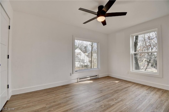 spare room featuring a healthy amount of sunlight, light wood finished floors, baseboards, and a baseboard heating unit