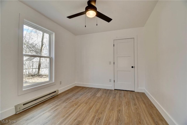 spare room featuring a ceiling fan, baseboard heating, light wood-style flooring, and baseboards