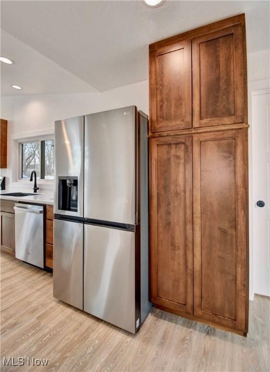 kitchen with appliances with stainless steel finishes, light countertops, a sink, and light wood-style flooring