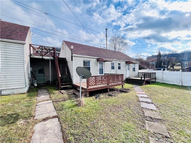 back of property with a shingled roof, a yard, a deck, and fence