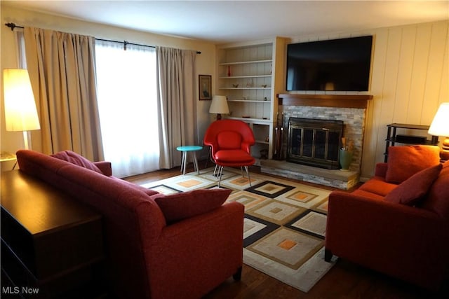 living area with built in shelves, a fireplace, and wood finished floors