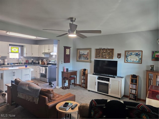 living area featuring light carpet, a ceiling fan, and baseboards