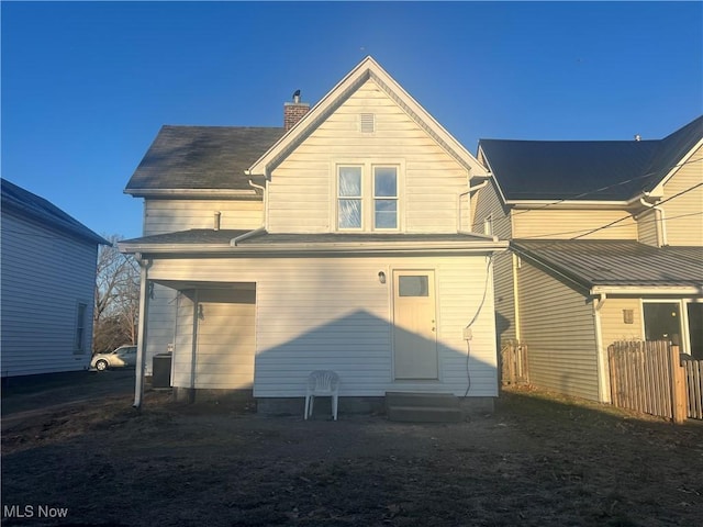 rear view of property with entry steps, a chimney, and fence