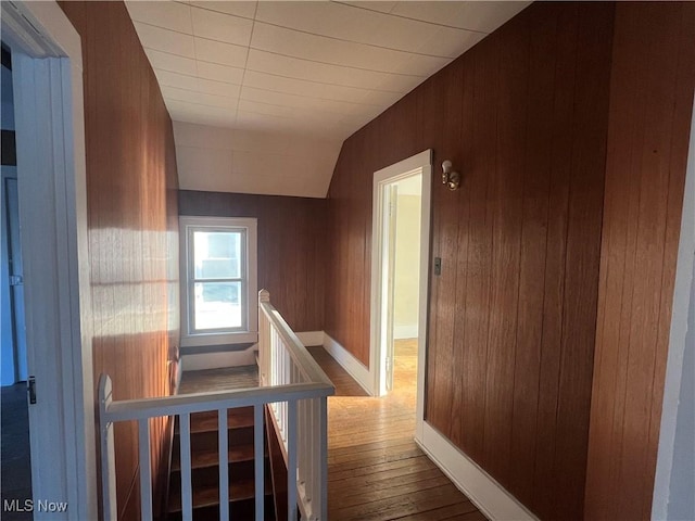 hallway with lofted ceiling, hardwood / wood-style flooring, wooden walls, an upstairs landing, and baseboards